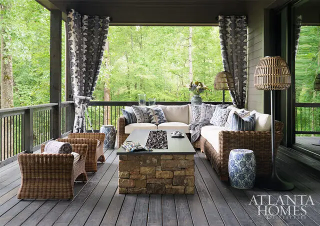 Covered porch with wicker sectional, stone fire pit table, and blue and white patterned pillows.
