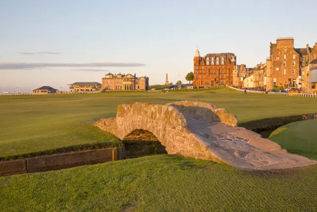 Stone bridge over a stream on a golf course with buildings in the background