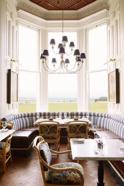 Restaurant dining area with bay windows, striped banquette seating, and floral upholstered chairs.