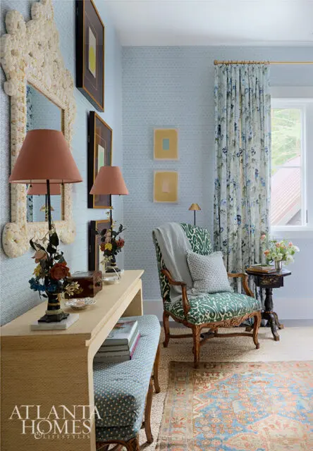 Light blue patterned wallpaper, console table with lamps, green patterned armchair, and floral