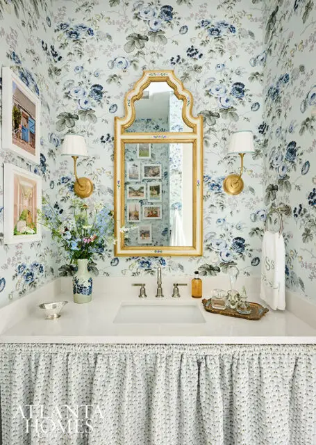 Powder room with blue floral wallpaper, gold mirror, and white vanity with skirt