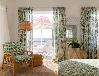Rattan armchair with green floral cushions, bamboo side table, and green floral curtains.