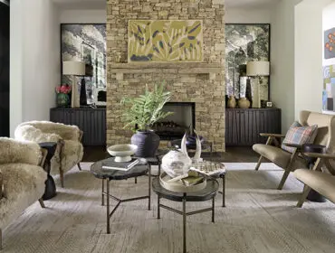 Living room with stone fireplace, textured rug, and plush armchairs.