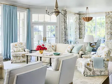 Living room with floral armchairs, light blue curtains, and a white sofa.