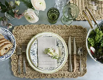 Table setting with woven placemats, blue and white floral plates, and green glassware.