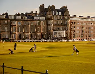 Golfers on a green course with a large stone building in the background.