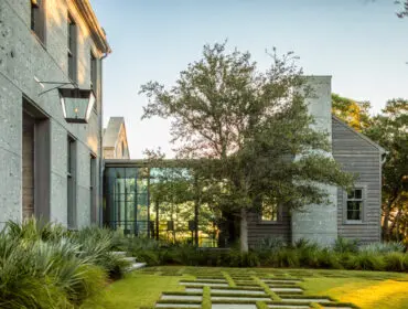 Modern home with gray stone and wood siding, glass walkway, and geometric lawn design.