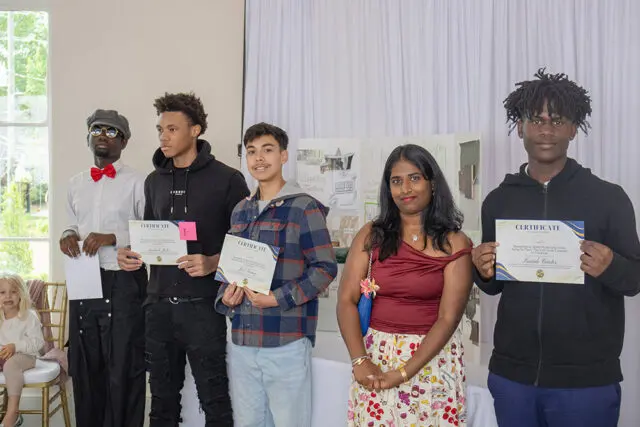 Five people stand holding certificates. A young girl sits to the left.