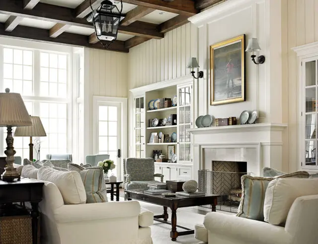 Living room with white sofas, patterned armchairs, fireplace, and built-in bookshelves.