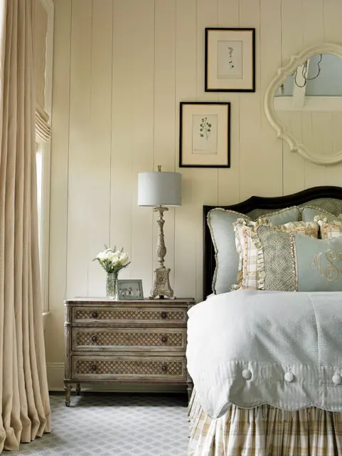 Bedroom with paneled walls, a vintage dresser, and a bed with blue and plaid linens.