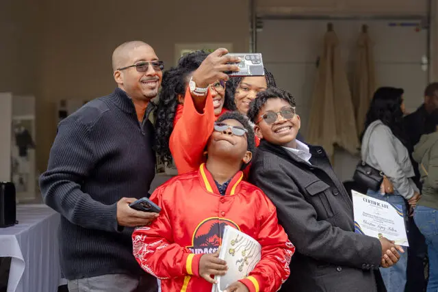 Family taking a selfie, one boy holds a certificate.