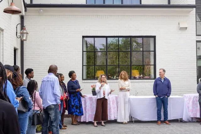 Group of people gathered outside a white brick building with a large window.