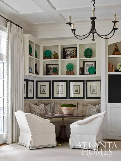 Built-in cream shelving with green decorative plates and framed art above banquette seating and two
