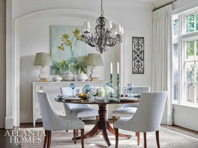 Dining room with round table, upholstered chairs, buffet, and abstract floral art.