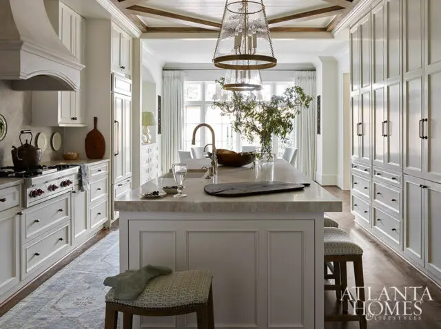 White kitchen with marble island, brass faucet, and paneled cabinetry. Wood ceiling beams.