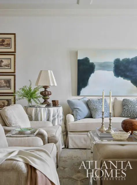 Living room with neutral upholstered furniture, blue patterned pillows, and landscape painting
