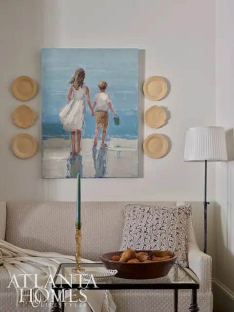 Painting of two children on a beach above a patterned sofa with a glass coffee table