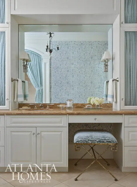 White vanity with marble countertop, blue patterned wallpaper, and gold stool