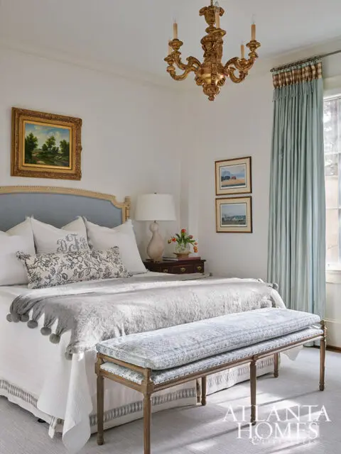 Bedroom with blue upholstered headboard, gray throw with pom-poms, and upholstered bench.