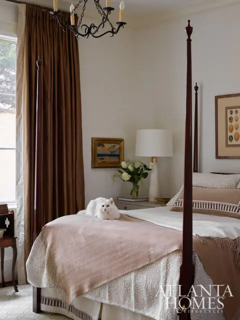 Bedroom with four-poster bed, white cat on pink blanket, and brown curtains.