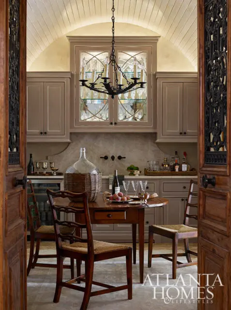 Tavern-style kitchen with taupe cabinetry, glass-fronted display cabinet, and a wooden table.