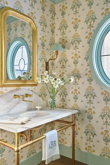 Powder room with floral wallpaper, marble vanity, brass fixtures, and oval windows.