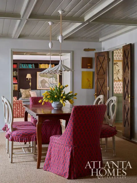 Dining room with wooden table, chairs in red floral slipcovers, and yellow tulips.