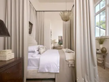 Bedroom with a four-poster bed, draped in cream curtains, and a decorative chandelier.