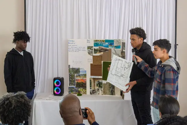 Two teenagers present an outdoor design project with mood boards and blueprints.