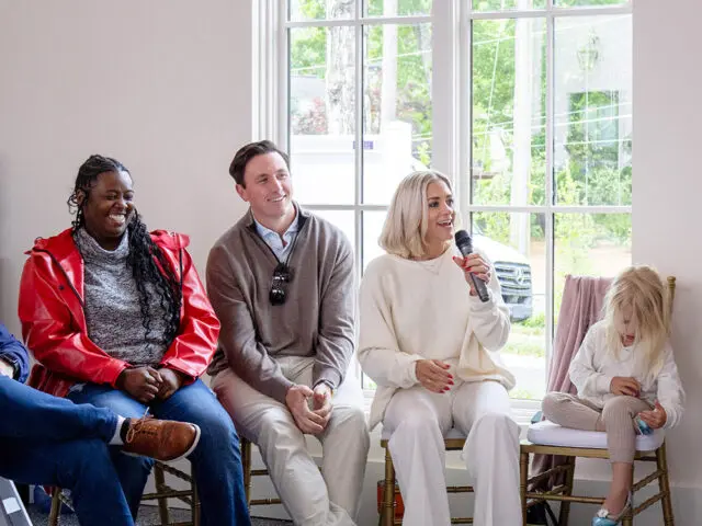Four people sitting in chairs in front of a large window. A woman speaks into a microphone.