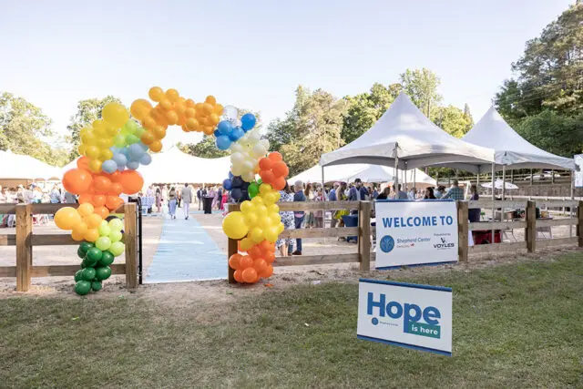 Rainbow balloon archway and tents at Shepherd Center Derby Day event. Sign reads 'Hope is here'.