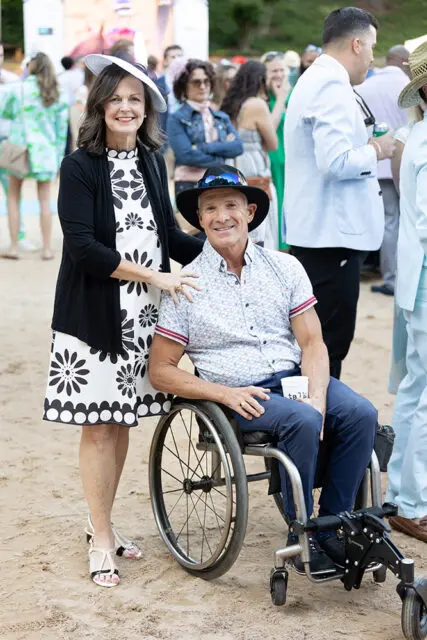 Woman in a black cardigan and floral dress stands next to a man in a wheelchair.