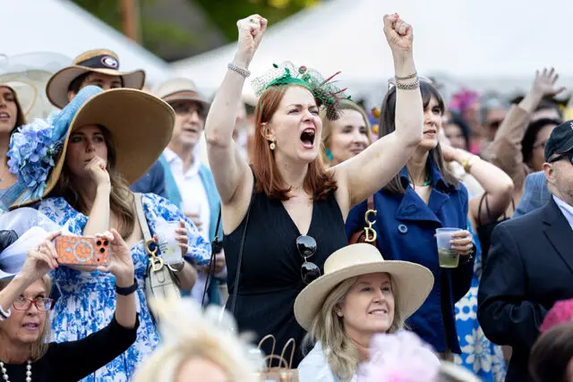 Crowd cheering at an event, some wearing hats and fascinators.