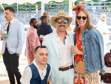 People in colorful attire at an outdoor event, some wearing hats and sunglasses.