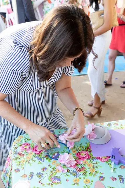 Woman in striped dress crafting with pink flowers and a grey hat