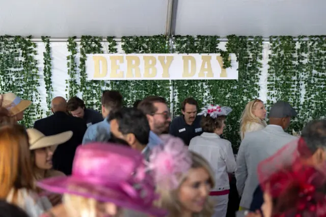 Gold letters spell DERBY DAY on a white sign against a backdrop of green ivy.