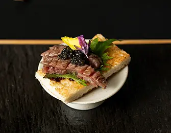 Seared beef slices with caviar and edible flowers on toast