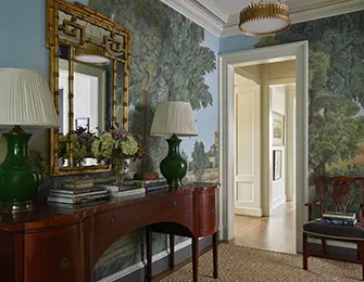 Entryway with scenic wallpaper, a mahogany console table, and two green lamps.