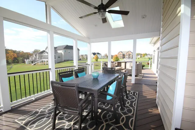 Screened porch with dark wood table and chairs, teal cushions, and outdoor rug.