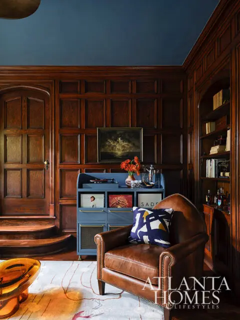 Study with dark wood paneling, blue ceiling, leather armchair, and blue record cabinet.