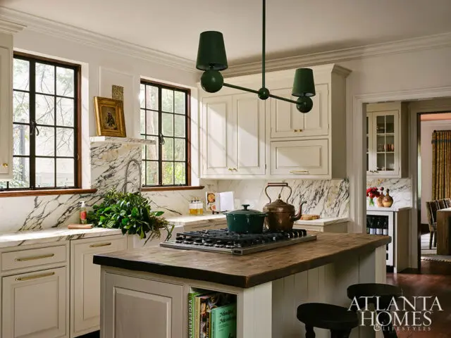 Cream kitchen with marble backsplash, dark windows, and a wooden island topped with a stovetop.