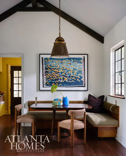 Dining nook with banquette seating, two chairs, and abstract art. Dark wood floors.