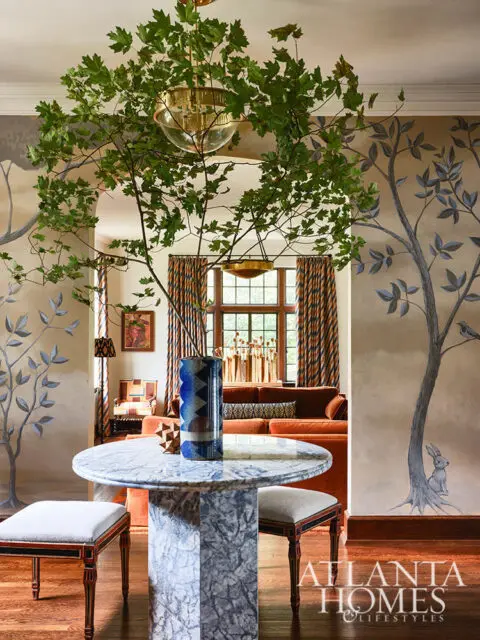 Marble pedestal table with two upholstered stools, orange sofa, and tree mural