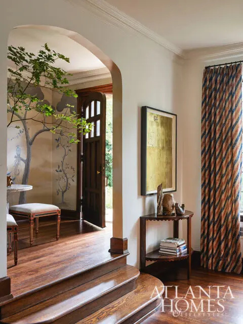 Entryway with arched doorway, mural wallpaper, wooden stairs, and striped curtains.