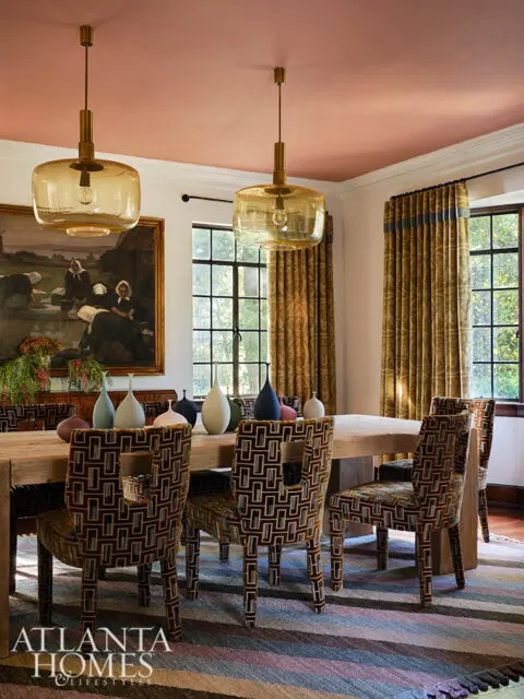 Dining room with wood table, patterned chairs, amber pendant lights, and striped rug.
