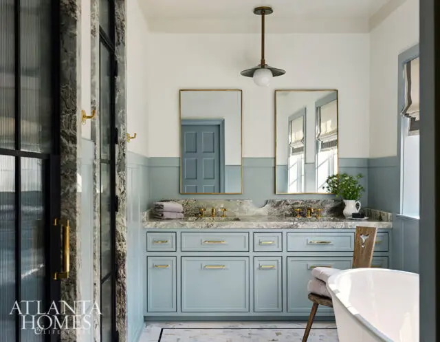 Light blue bathroom vanity with marble countertop, brass hardware, and two mirrors.