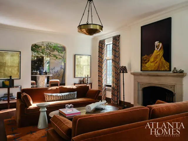 Living room with rust-colored sofas, arched doorway to dining area, fireplace, and artwork.