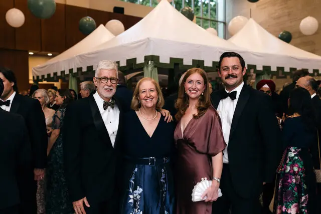Four people in formal wear posing in front of a tent structure with balloons