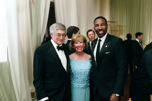 Man in tuxedo with bow tie, woman in blue dress, man in tuxedo