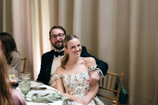 Man in tuxedo and woman in floral dress smiling at a formal event